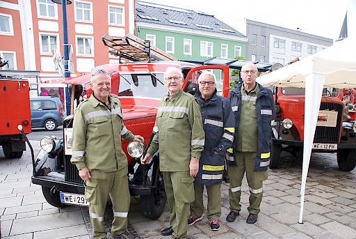 Altbürgermeister Dr. Peter Koits mit Kollegen präsentieren Oldtimer Feuerwehrautos.